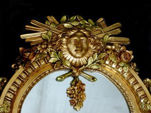 Top half of ornate gold mirror with an abstract gold face on the frame