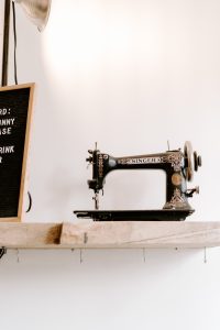 Antique black and gold singer sewing machine on a wooden shelf next to a chalkboard