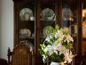 Dark wood china cabinet with a vase with white lilies in the foreground.