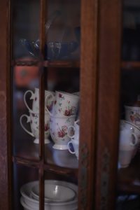 Closeup image of floral china teacups inside a wooden china cabinet