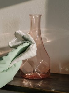 Gloved hand cleaning a vase with a cloth.