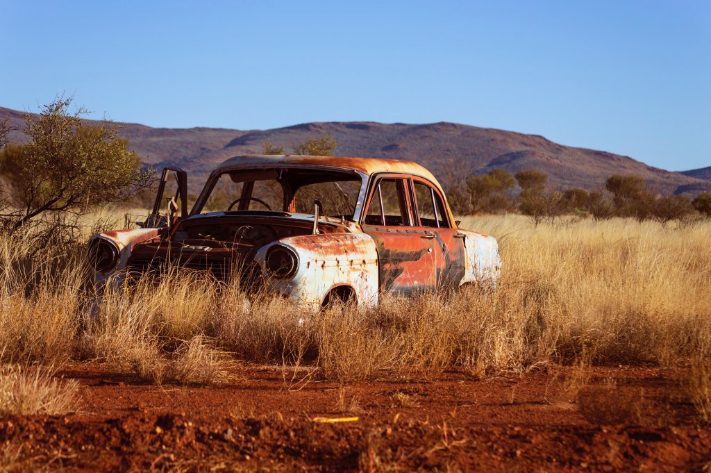 Rusted car surrounded by tall yellow prairie grass with hills in the background