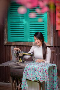 Young woman smiling while using an antique singer sewing machine to sew a floral cloth