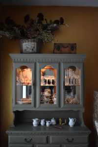 Gray painted china cabinet with illuminated glasses and dishes inside